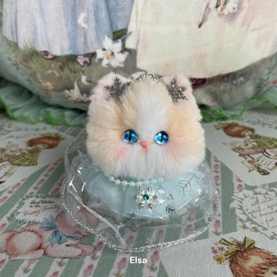 Handmade plush kitten from Fairy Paws Collection with blue eyes, star crown, pearl necklace, and floral background.