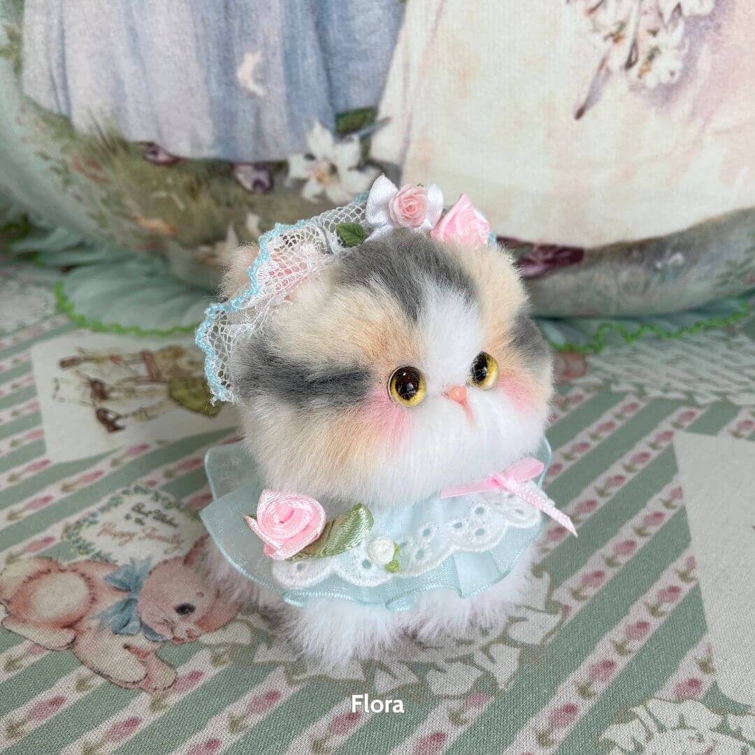 Adorable handmade kitten from Blossom Kitten Collection, featuring pastel colors, bows, and lace, posing cutely in floral decor.