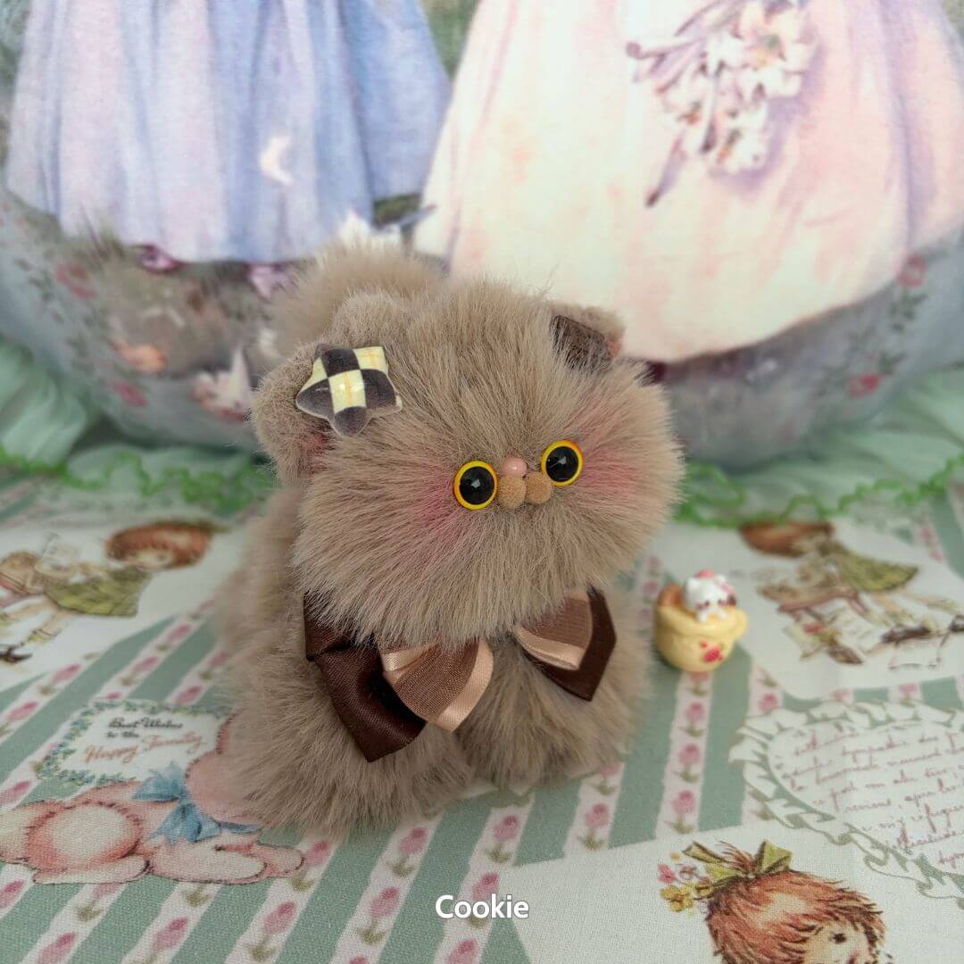 Fluffy Kitten Collection: Cute brown fluffy cat figurine with bow and rosy cheeks, surrounded by playful decorations.