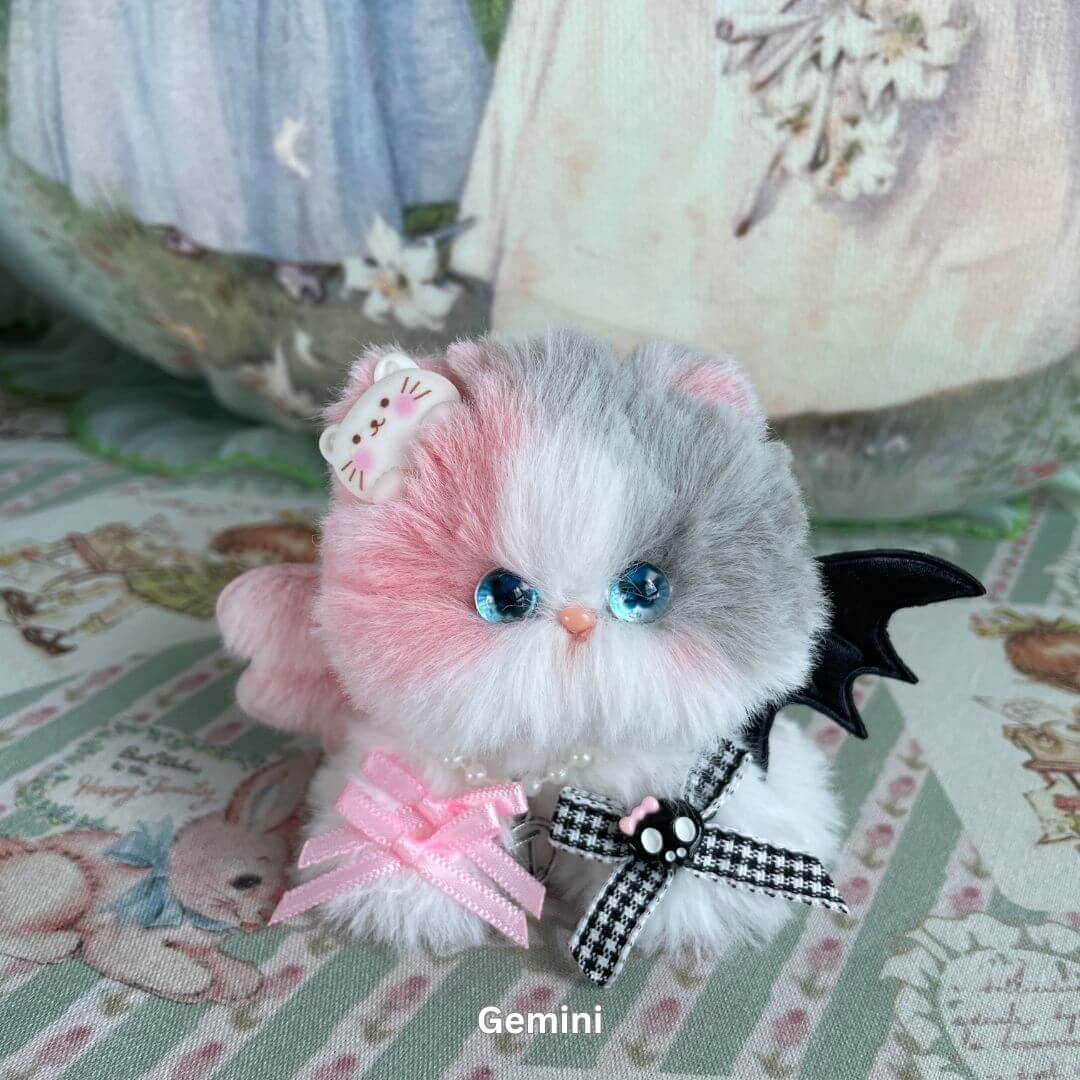 Gemini-inspired plush kitten with pink and gray faux fur, adorned with ribbons and charms, part of the Zodiac Kitten Collection.