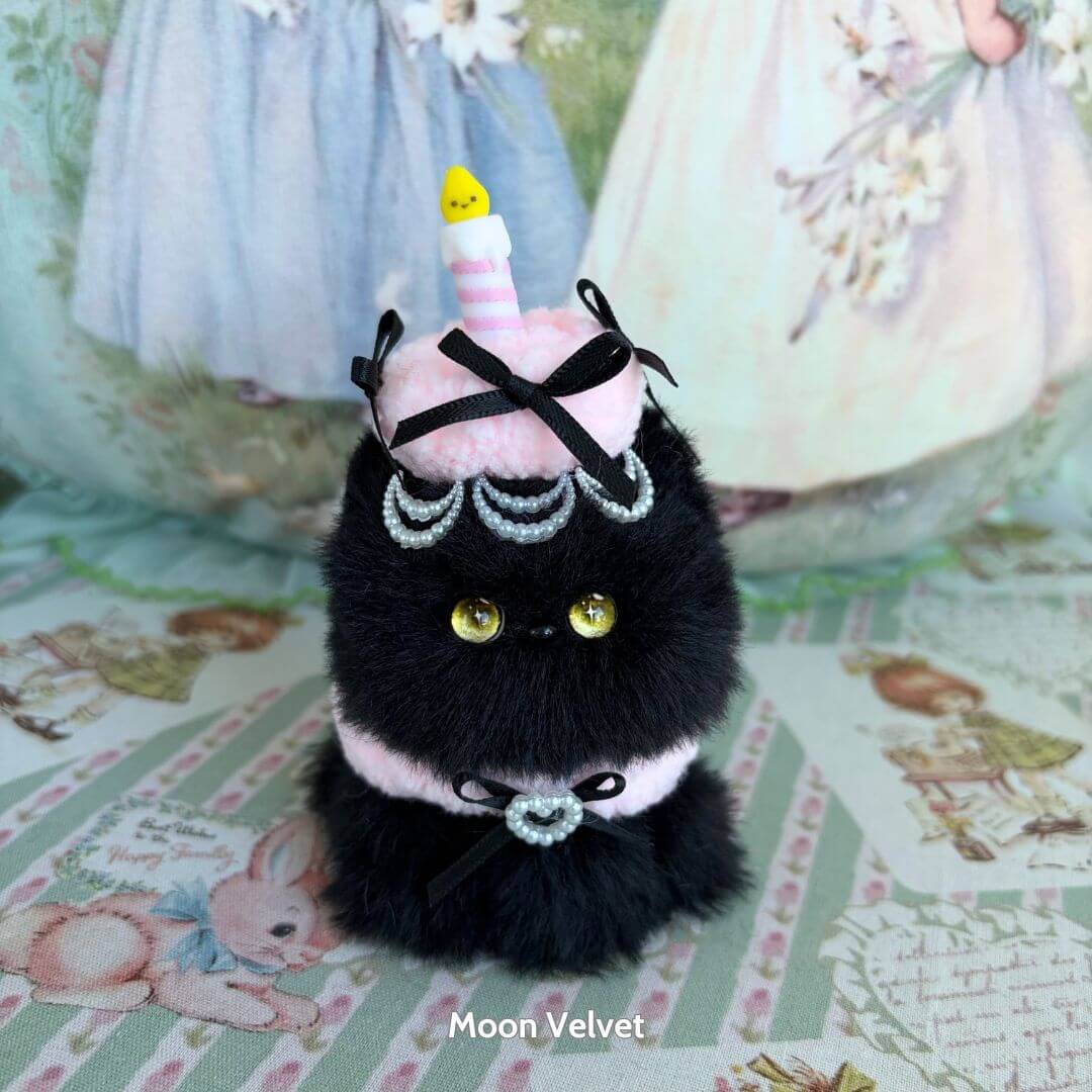 Handmade kitten from Mewlicious Collection, black fluffy figurine dressed as a cake with pink icing and a candle, cute animal collectible.
