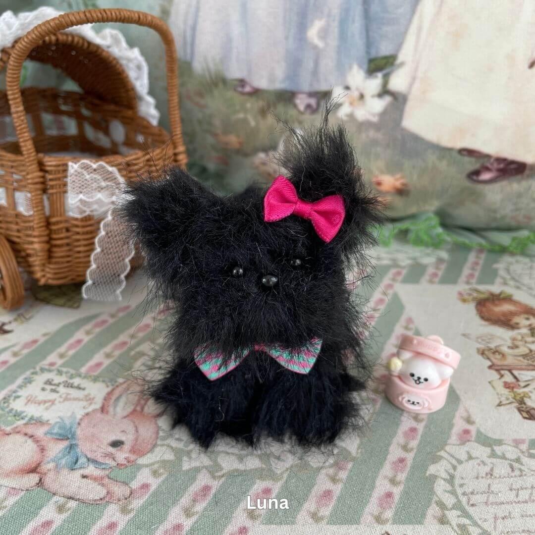 Handmade toy dog with black faux fur, pink ribbon bow, and dessert accessory from the Fluffy Puppy Collection displayed with basket.
