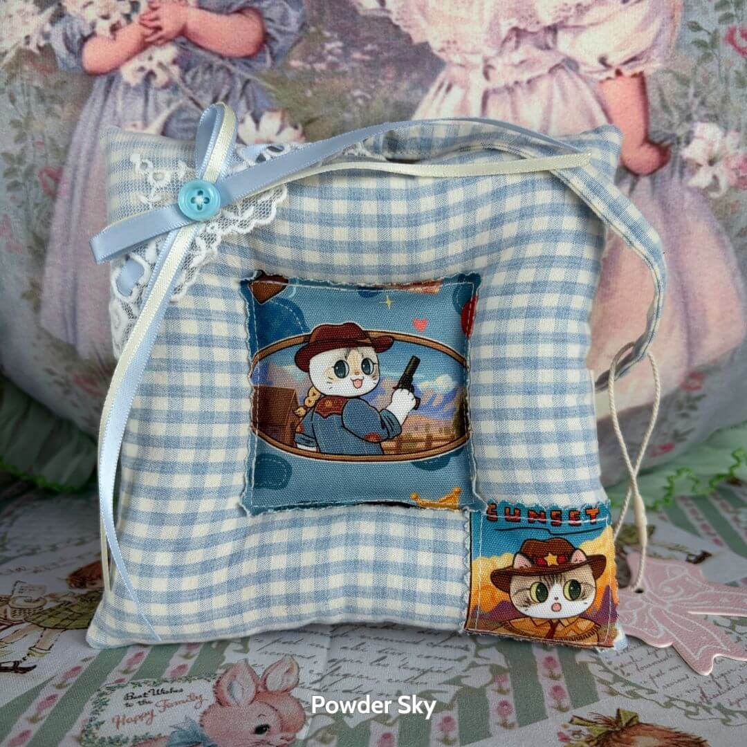 Handmade cushion with cute cat character artwork, blue checkered design, ribbon detail, and whimsical touch for decor.