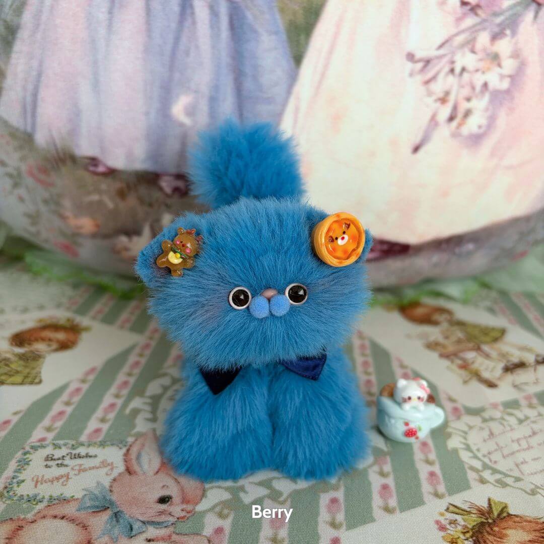 Cute handmade kitten from the Fruity Kitten Collection, fluffy blue with fruit-themed accessories and bow, posing adorably.