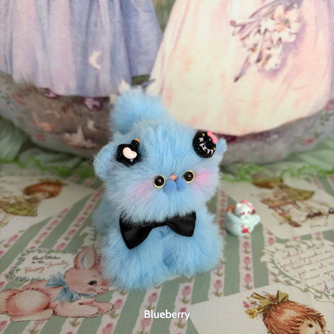 Adorable blue handmade kitten from the Fruity Kitten Collection, featuring a black bow, cheerful expression, and cute accessories.