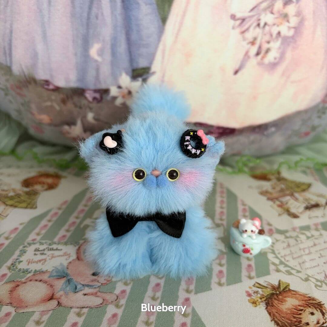 Cute handmade kitten from the Fruity Kitten Collection, fluffy blue with a black bow and playful accessories, kawaii design.