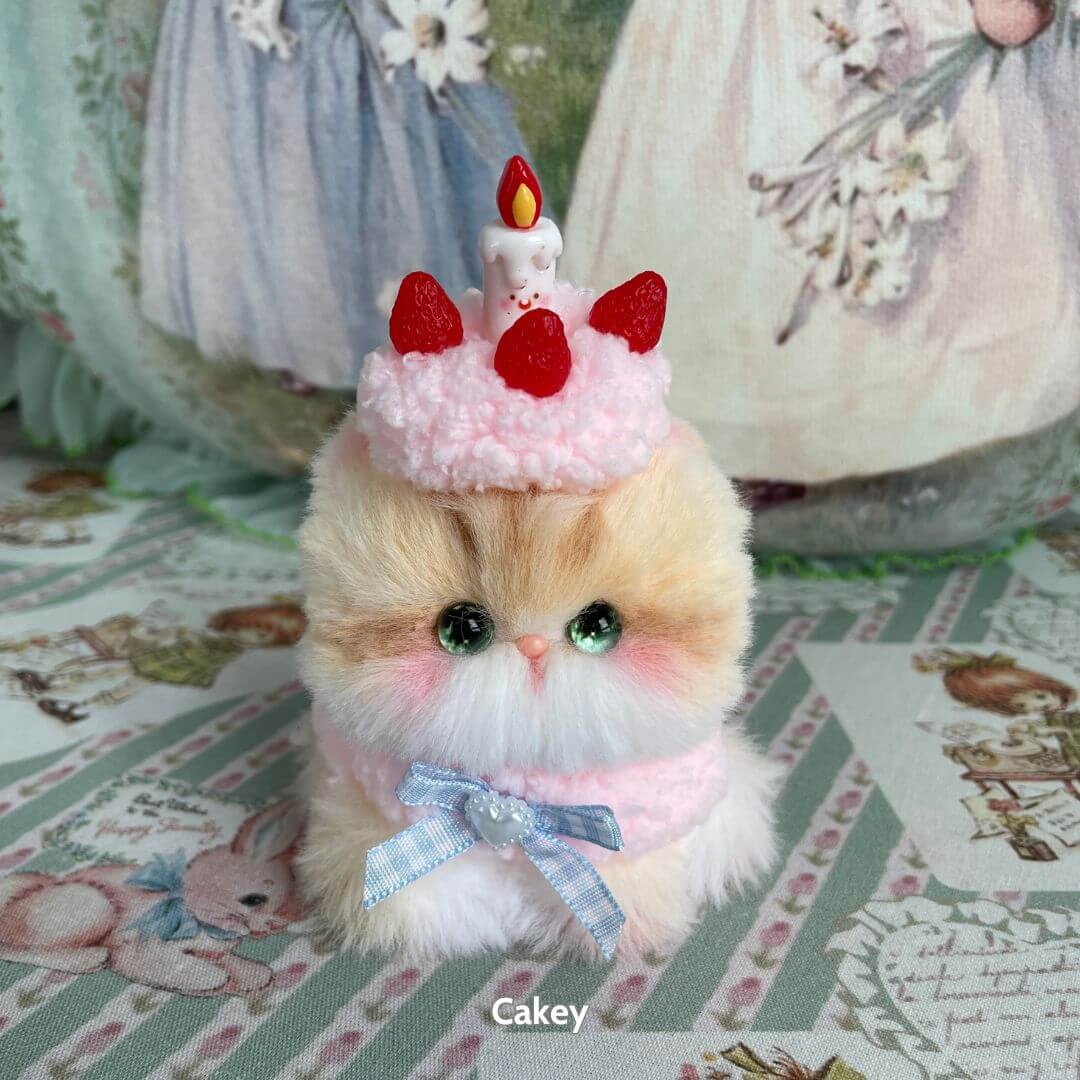 Handmade kitten from the Mewlicious Collection, fluffy cat figurine wearing a pink frosting crown with a candle and strawberries.