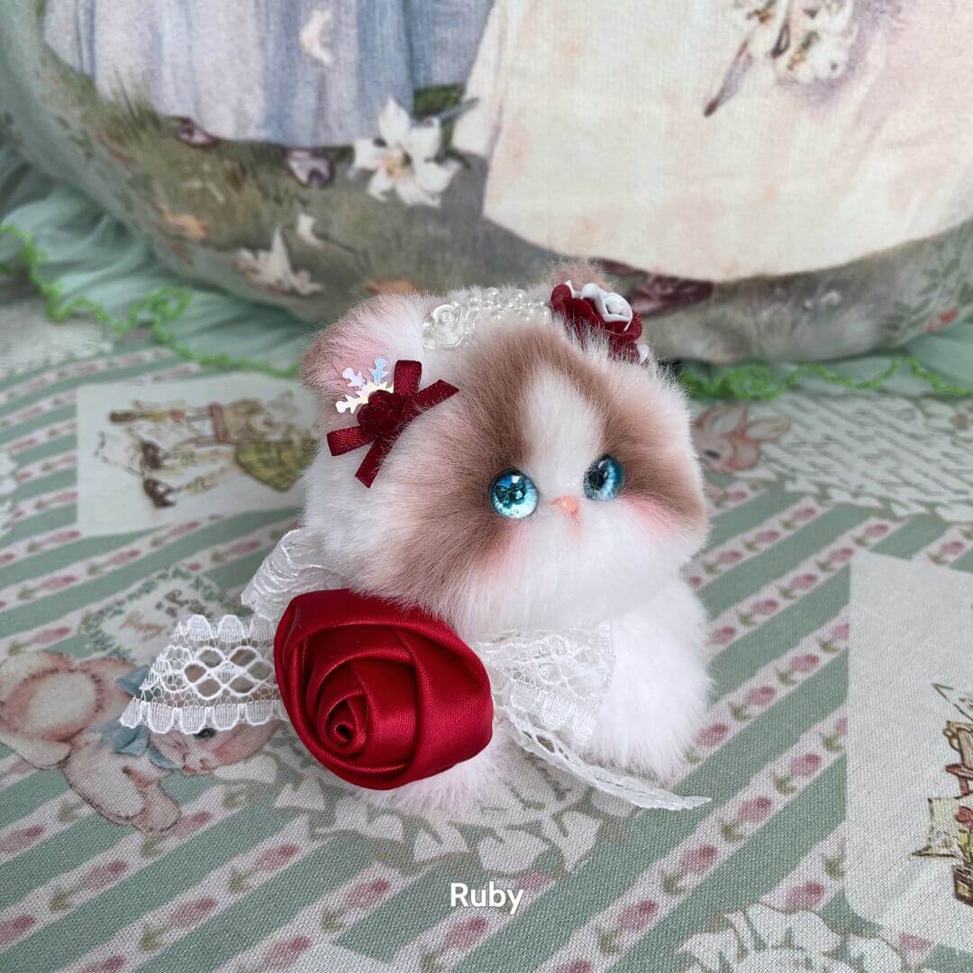 Adorable handmade kitten from the Blossom Kitten Collection, featuring fluffy white fur, blue eyes, and red floral accessories.