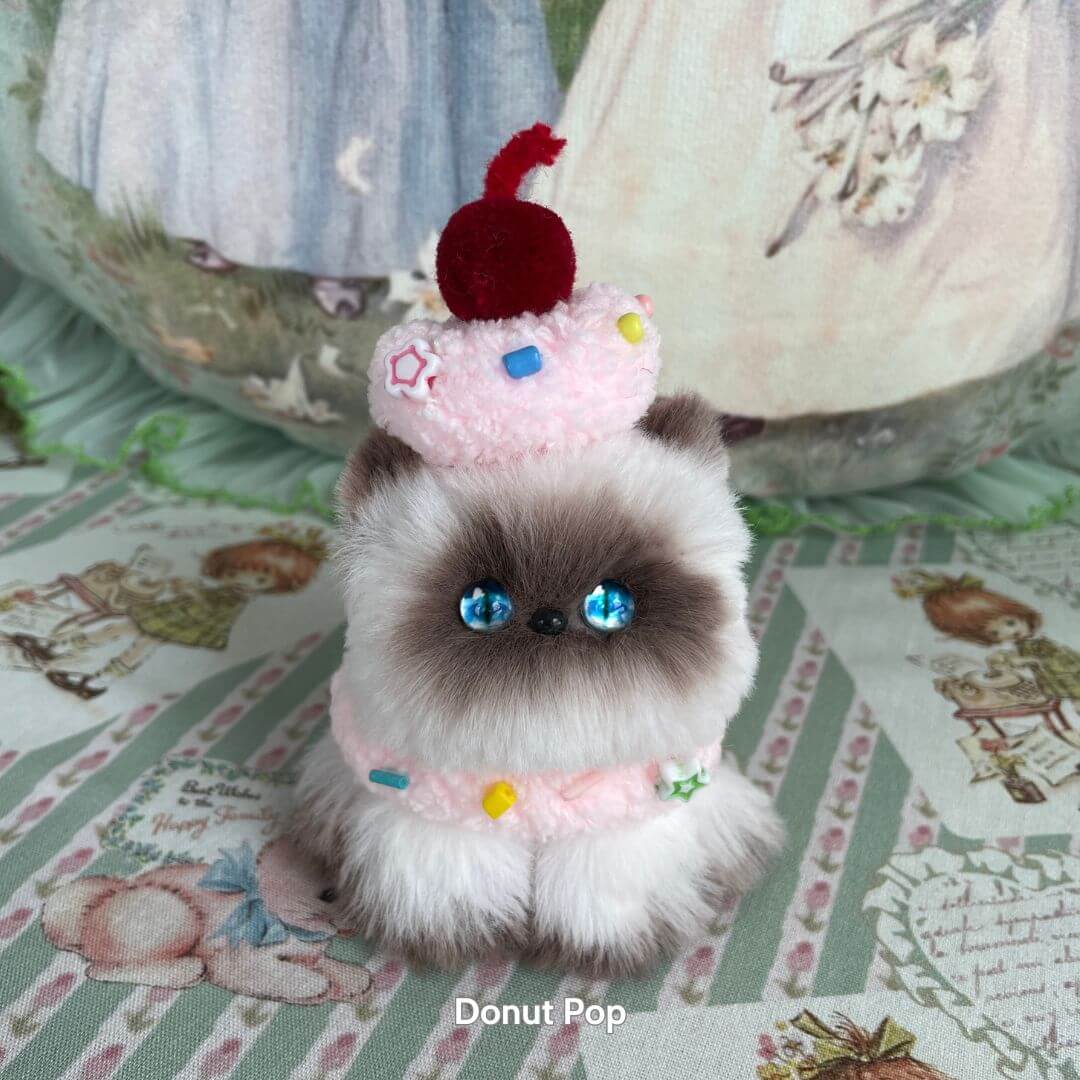 Handmade kitten from the Mewlicious Collection, fluffy cat figurine with a donut hat and blue eyes, cute animal collectible.