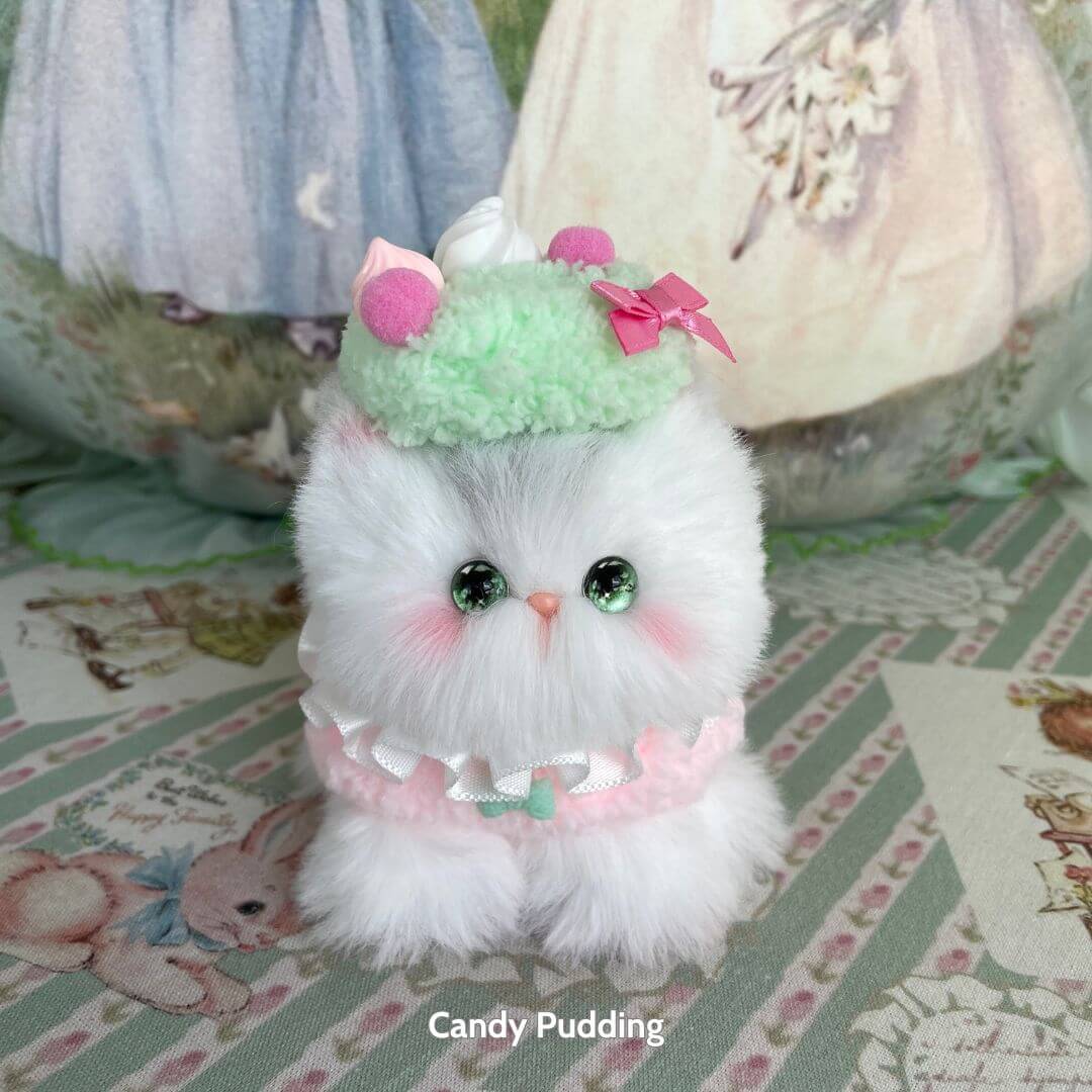 Handmade kitten from Mewlicious Collection, fluffy white cat figurine with a pastel green dessert hat and pink bow, cute and collectible.