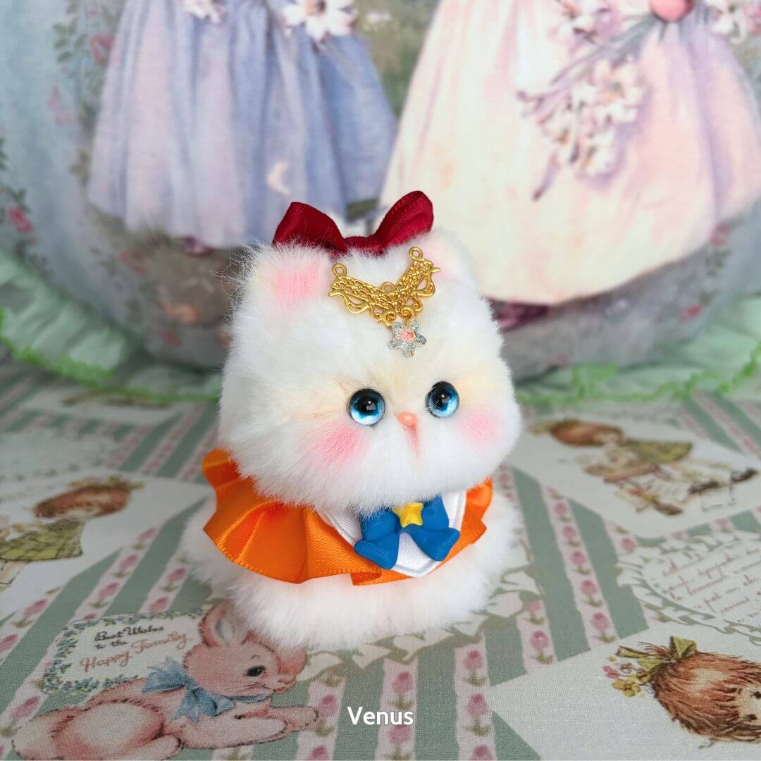 Handmade kitten from Moonbound Companions, fluffy white figurine with blue eyes, orange bow and crown, cute kawaii style.