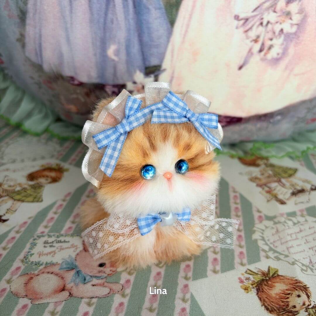 Adorable fluffy kitten from the Fairy Paws Collection, wearing a blue plaid bow and lace accessories, hand-painted features.
