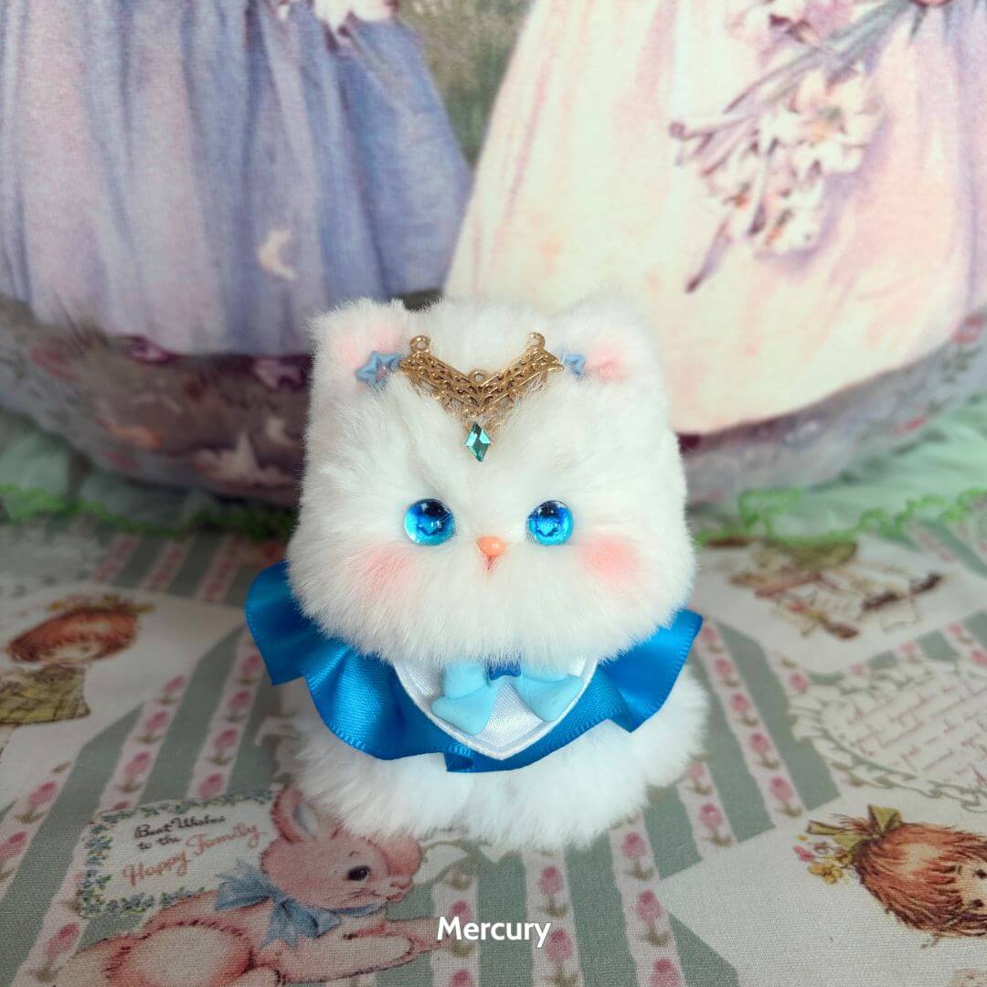 Moonbound Companions fluffy kitten figurine in blue attire with a crown, featuring bright blue eyes and soft white fur.