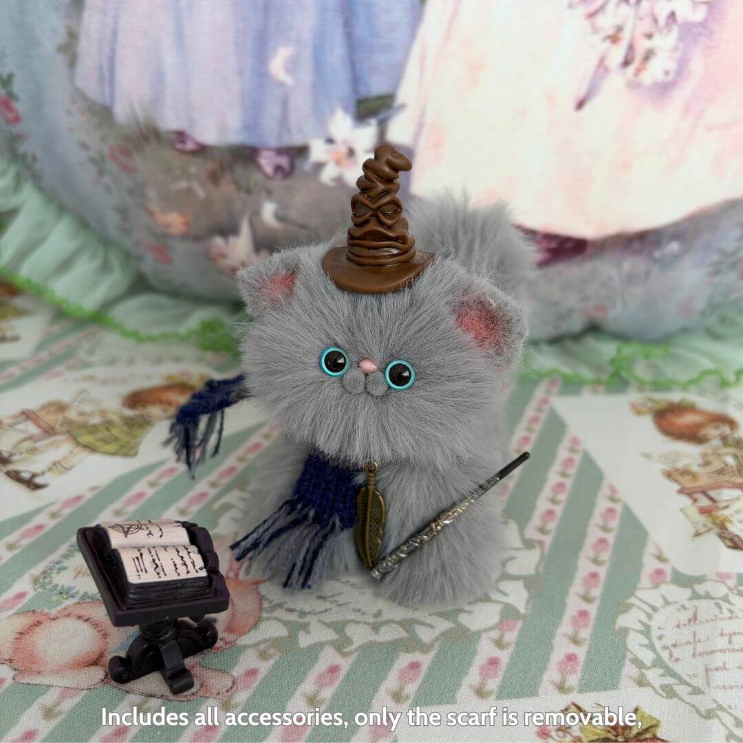 Fluffy grey handmade kitten wearing a wizard hat, holding a wand, next to a scroll, part of Magic Kitty Companions collection.