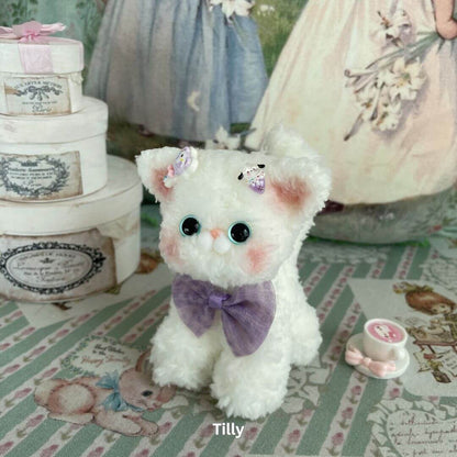 Handmade plush Devon Rex kitten toy with a purple bow, soft faux fur, and charming ears, surrounded by vintage decor.