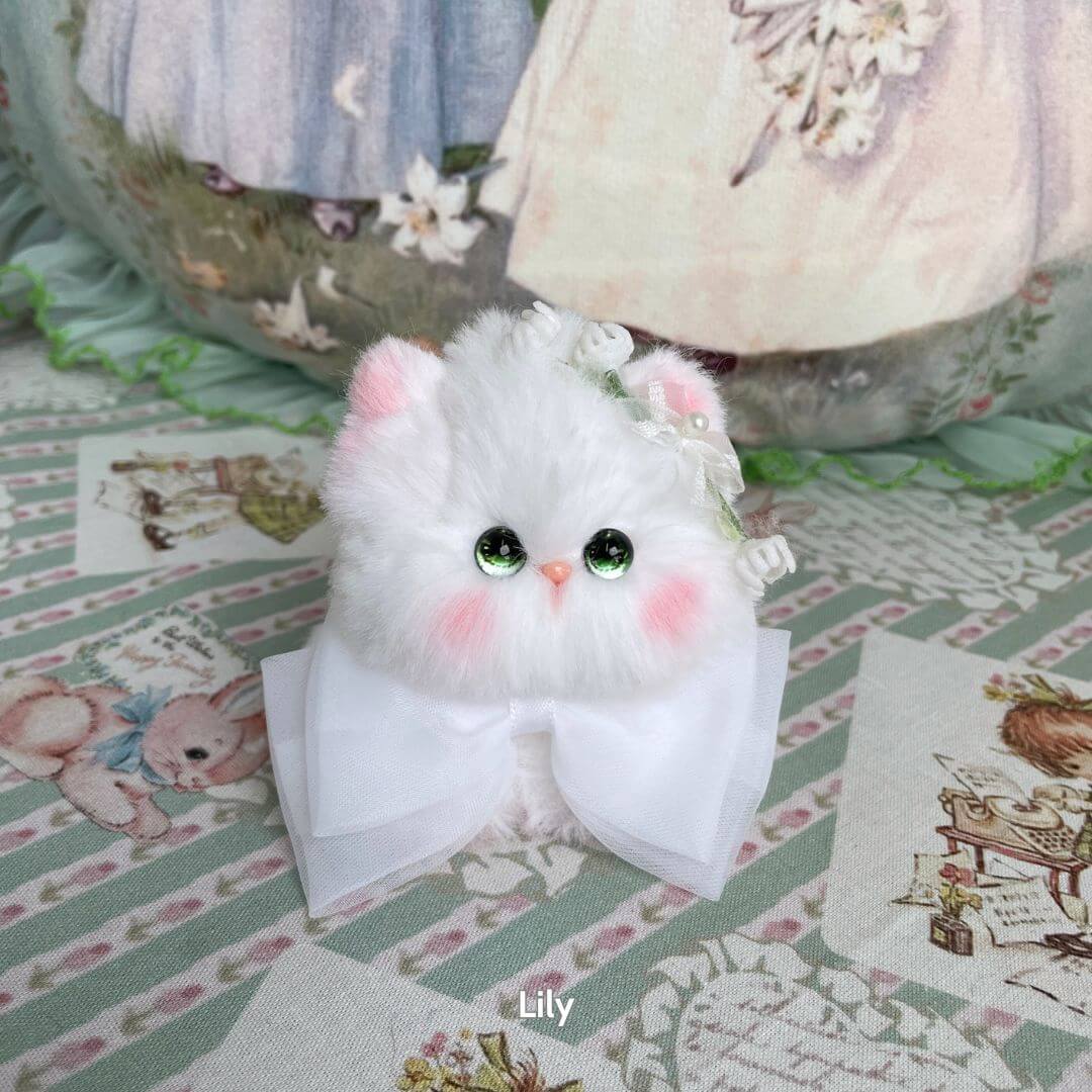 Adorable handmade kitten from the Blossom Kitten Collection, featuring fluffy white fur, a large white bow, and charming green eyes.