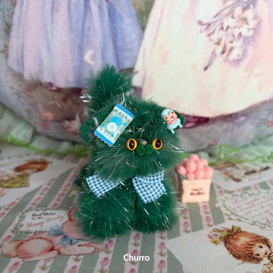 Handmade kitten in green faux fur, adorned with blue bows and accessories, holding a note in the Twinkling Kitten Collection.