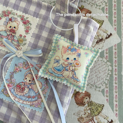 Cute cat-themed handmade sachet pillow with floral design, blue ribbon, and detachable pendant on vintage patterned fabric background.