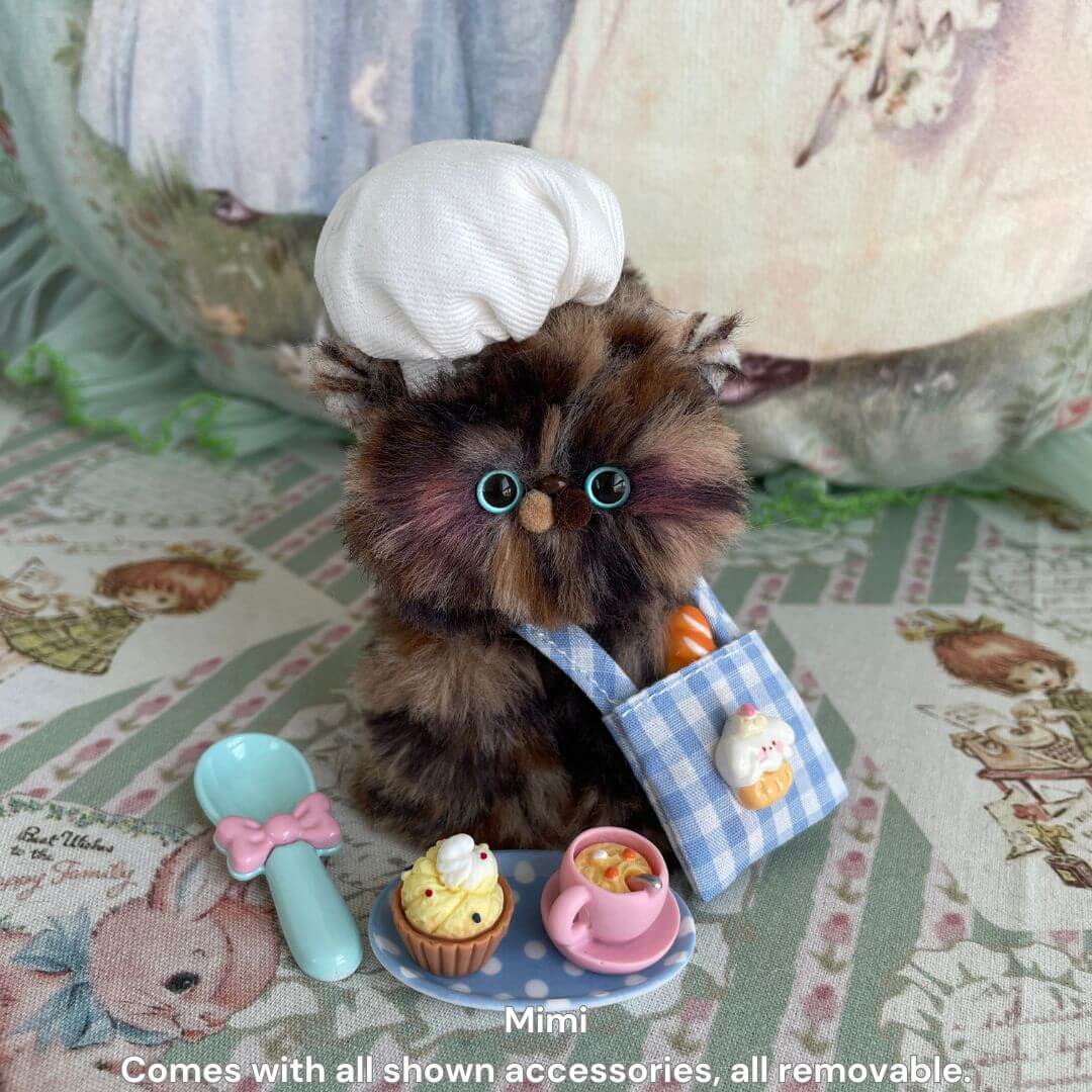 Cute handmade kitten chef with fluffy fur, wearing a white chef hat, surrounded by miniature cooking tools in Purrfect Chef Kitten Sets.
