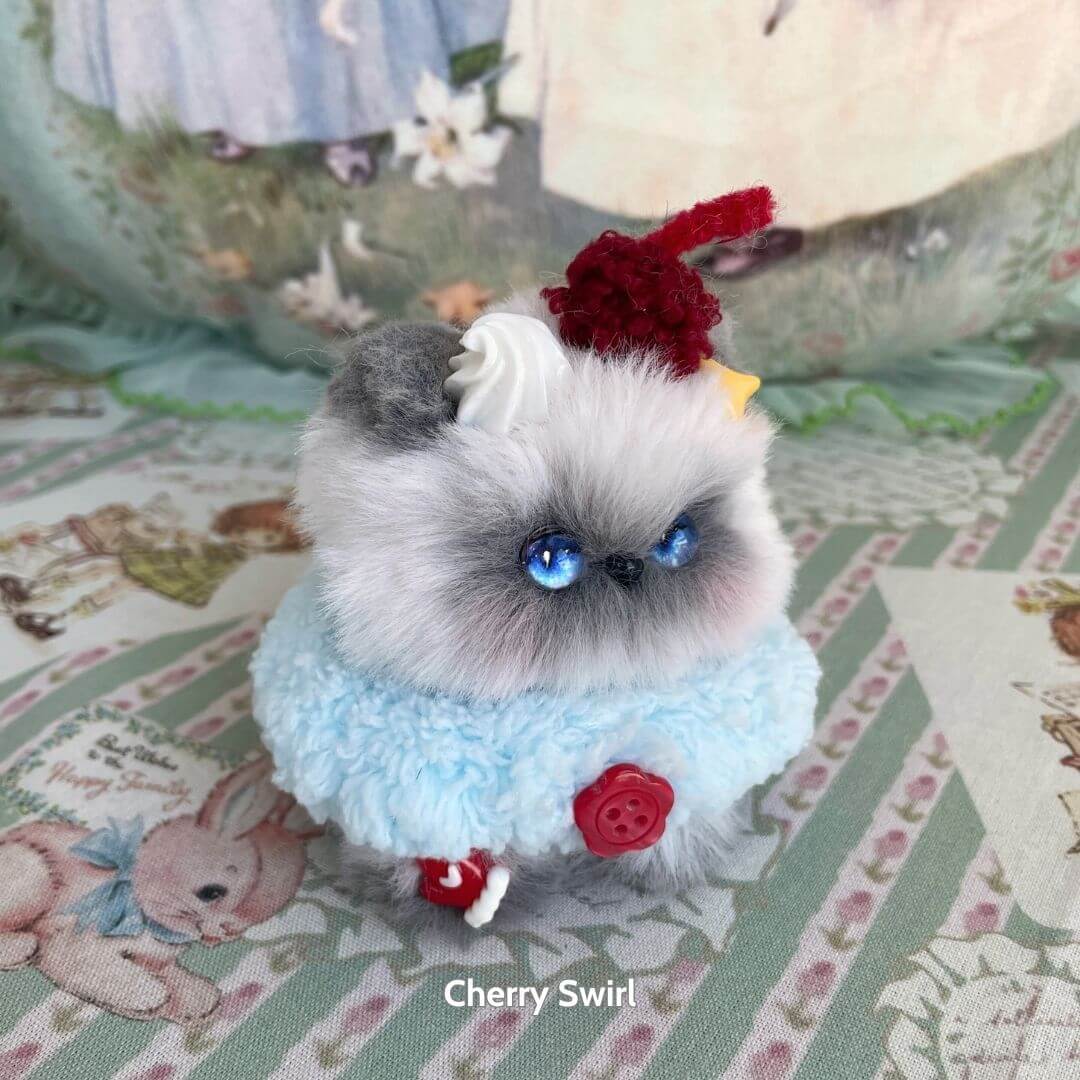 Handmade kitten in blue fluff, adorned with cherry and cream, resembling dessert; part of the Mewlicious Collection.