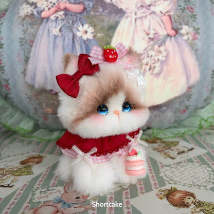 Adorable miniature kitten from the Enchanted Big Paws Collection, featuring fluffy fur, red accessories, and a cute dessert.