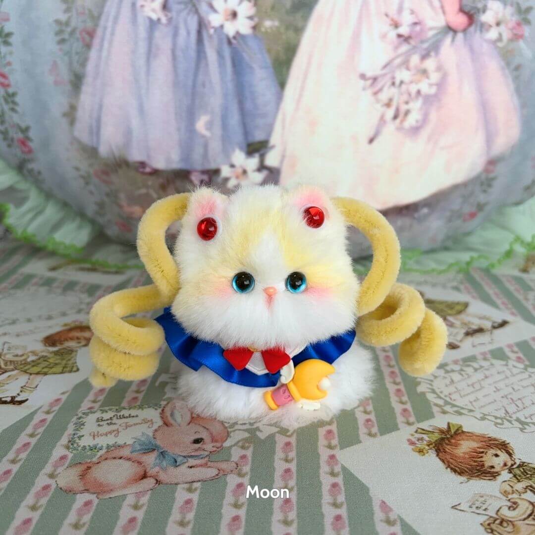 Handmade kitten from Moonbound Companions, featuring fluffy yellow fur, blue ribbon, and playful pipe cleaner accessories.