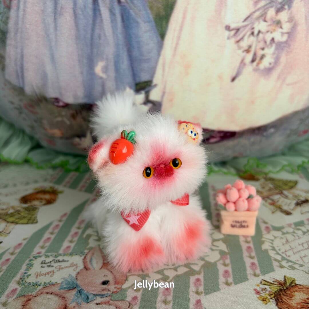 Handmade kitten from the Sweet Dreams Kitten Collection with pink and white fur, wearing a cherry accessory and bows, in a cute pose.