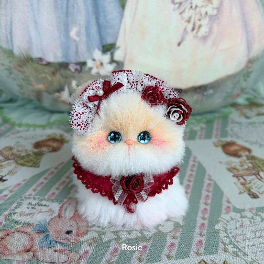 Adorable handmade kitten from the Blossom Kitten Collection, featuring a fluffy white body, blue eyes, and floral accessories.
