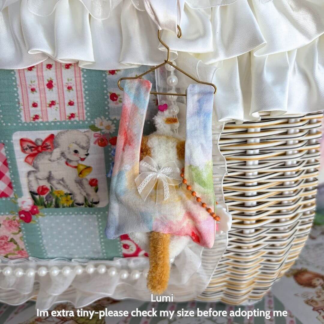 Little Hanger Pals, tiny handmade kitten in colorful fabric, softly hanging from a miniature hanger, cute animal collectible.