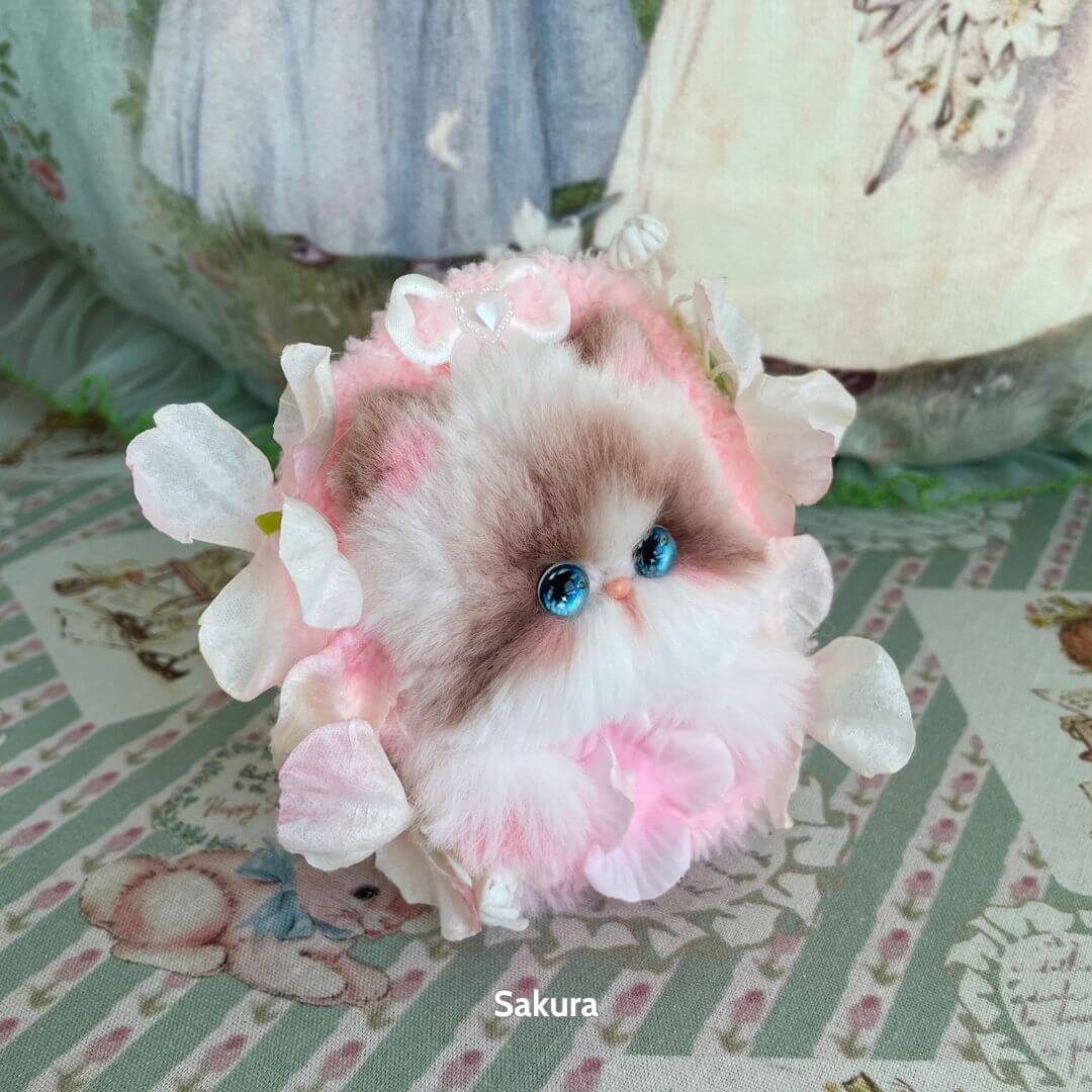 Adorable handmade kitten from the Blossom Kitten Collection, featuring fluffy fur, blue eyes, and floral accents in pink.
