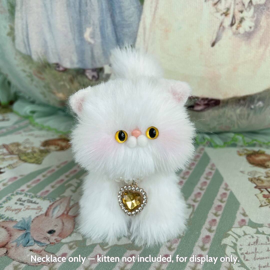 Miniature kitten figurine with fluffy white fur, wearing an Elegant Heart Necklace featuring a sparkling heart pendant.