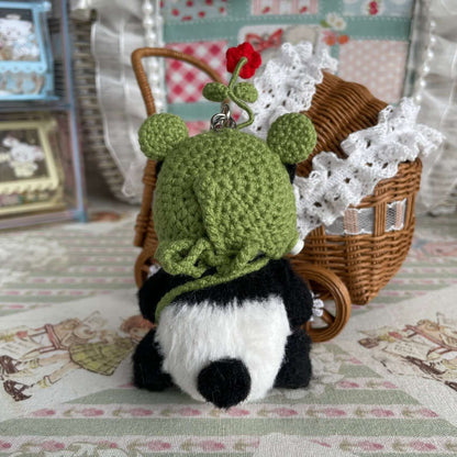 Handcrafted movable panda toy with green hat and handmade accessories, displayed next to a wicker basket on a decorative background.