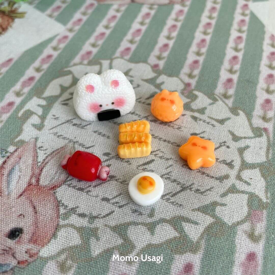 Mini Cat Bento Box featuring a cute fluffy kitten onigiri and colorful miniature food pieces on a floral patterned backdrop.