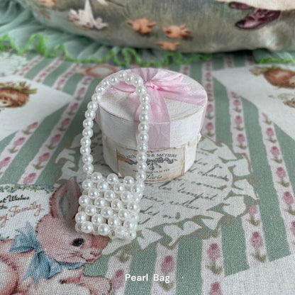 White pearl mini bag for plush toys, ideal as a stylish accessory for kittens or puppies, placed on a decorative floral background.