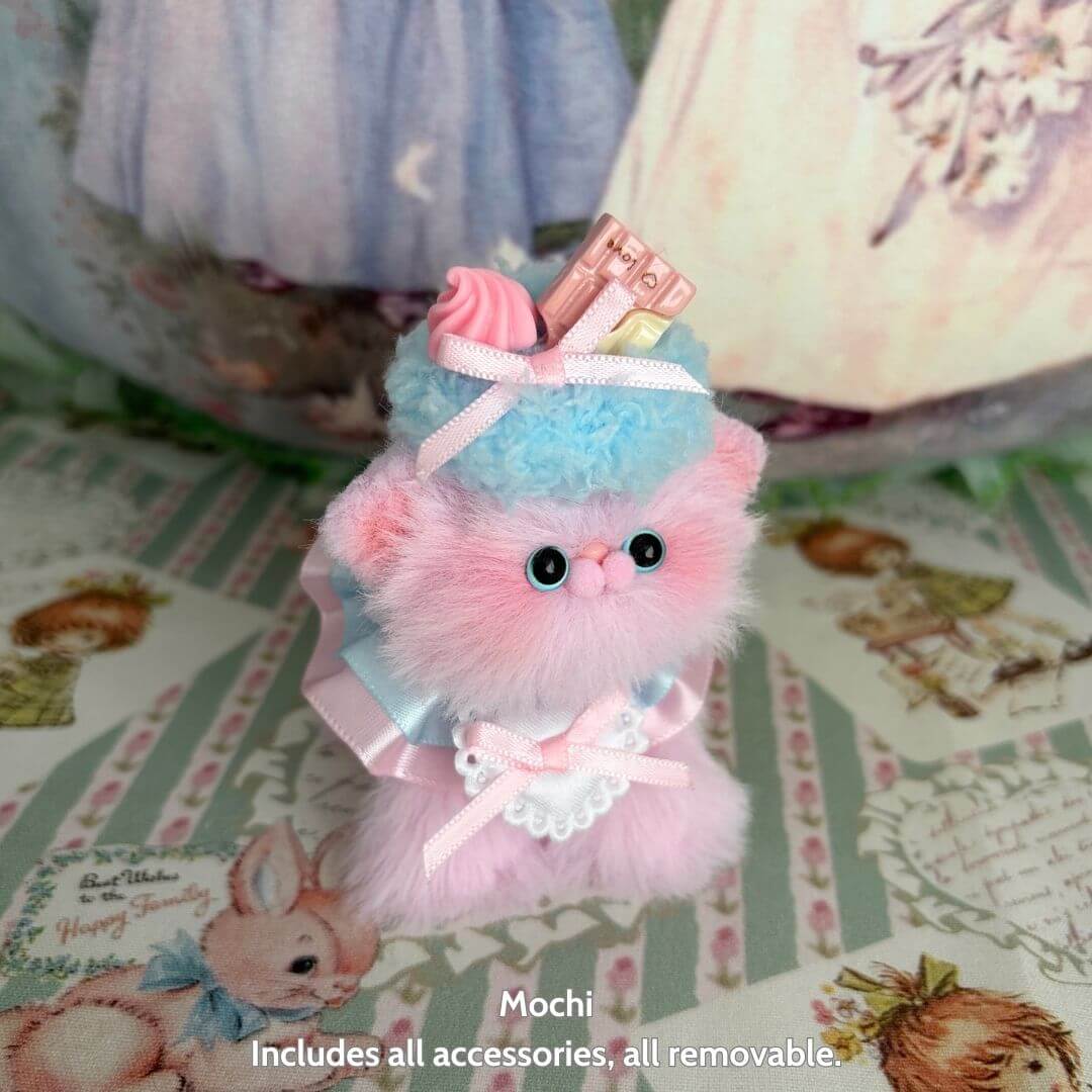 Sweet Treat Kitties handmade kitten with pink and blue fur, dessert-themed accessories, standing cutely on patterned background.