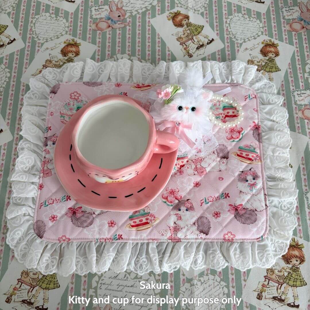 Handmade Sweet Tea Mat featuring a pink cup with a kitten figurine, decorated with lace and cute pastel patterns.