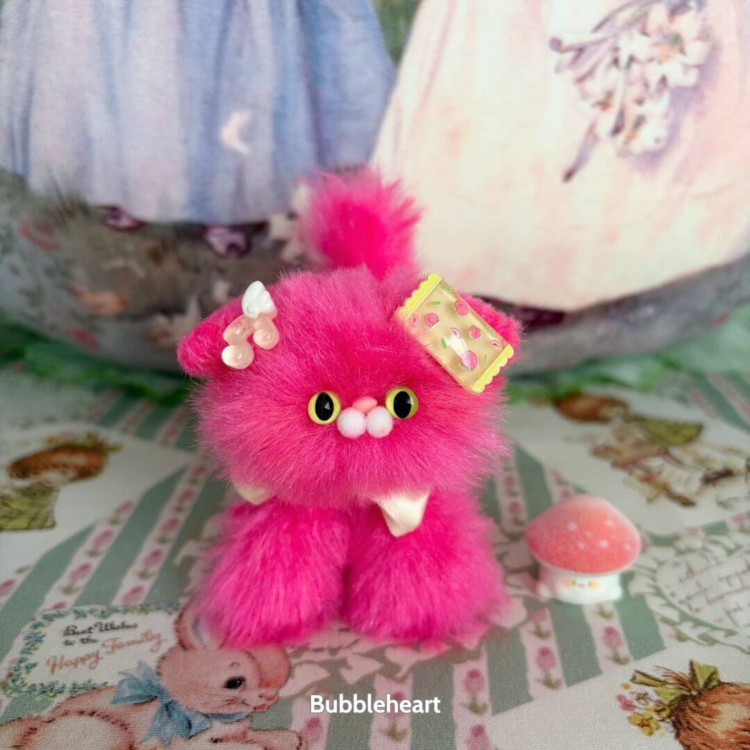 Alt Tag: Handmade kitten from the Glossy Meowgic Collection, featuring fluffy pink fur and a playful yellow accessory.