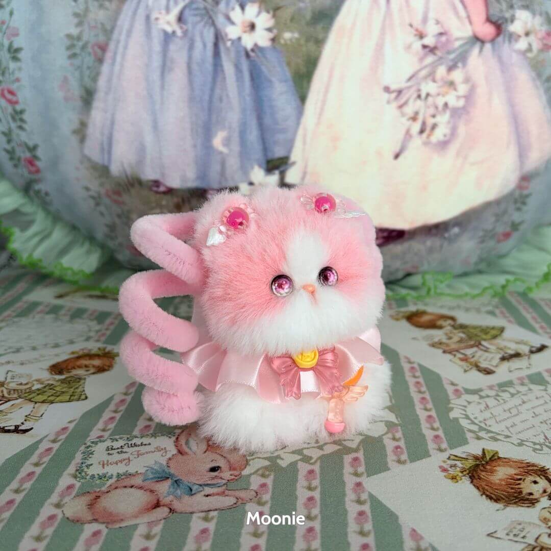 Alt Tag: Handmade kitten named Moonbound Companions, fluffy pink kawaii cat with accessories on decorative background.