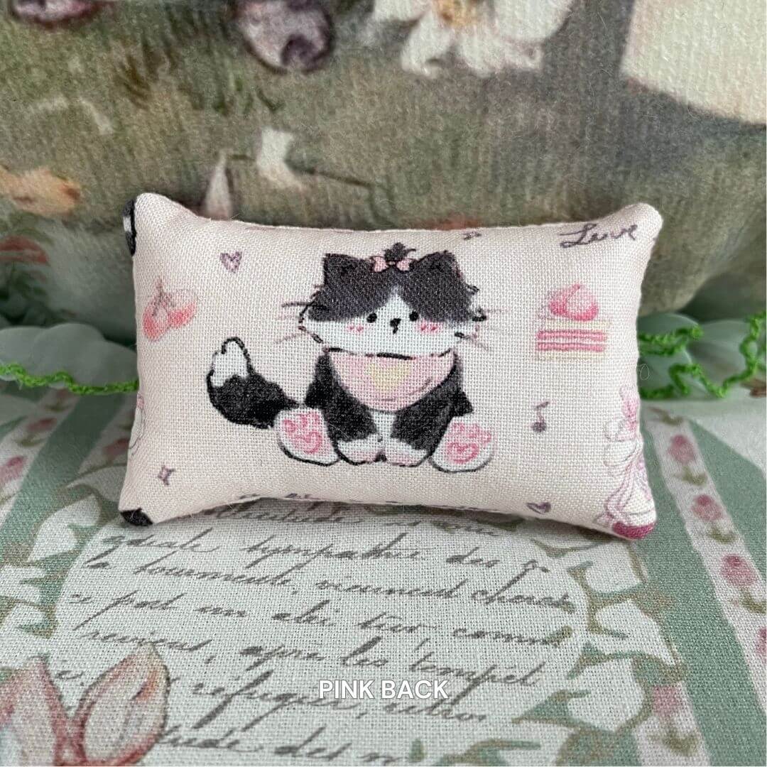 Handmade mini pillow with cute cat design, perfect for decorating miniature settings; ideal accessory for doll's homes.