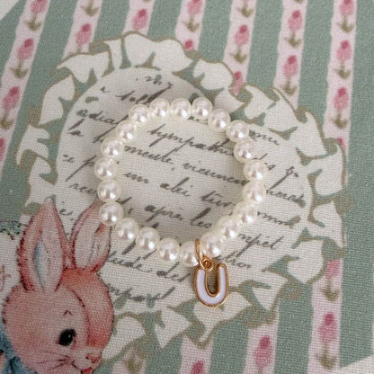 Initial Pearl Necklace featuring faux pearls and a delicate letter charm on a pastel floral background.