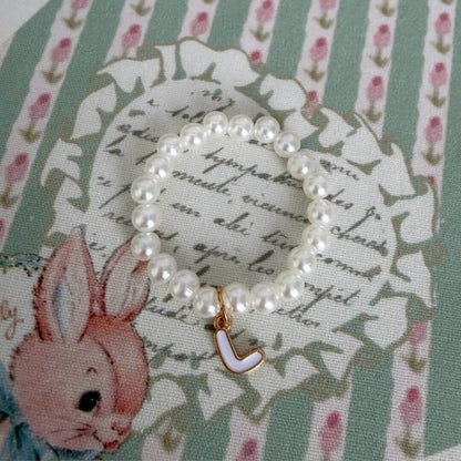 Initial Pearl Necklace featuring faux pearls and a delicate letter charm on a patterned fabric background.