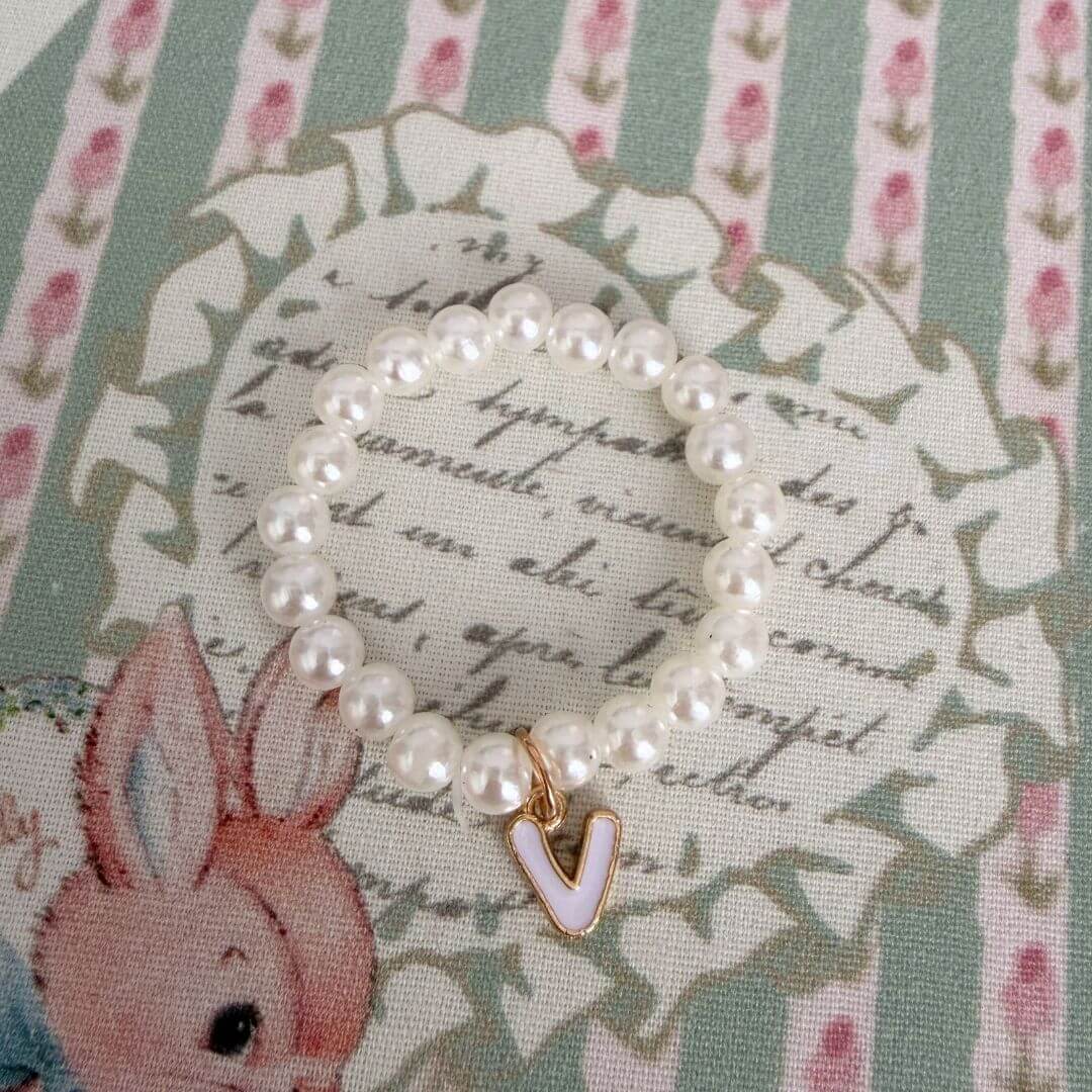 Initial Pearl Necklace with faux pearls and a delicate 'V' charm on a floral background, perfect for personal expression.