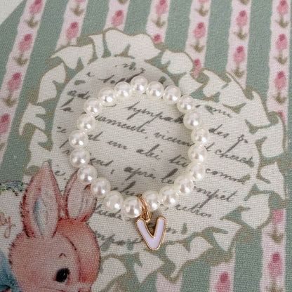 Initial Pearl Necklace with faux pearls and a delicate 'V' charm on a floral background, perfect for personal expression.
