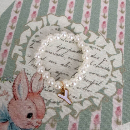 Initial Pearl Necklace with soft faux pearls and delicate letter charm on floral patterned background.