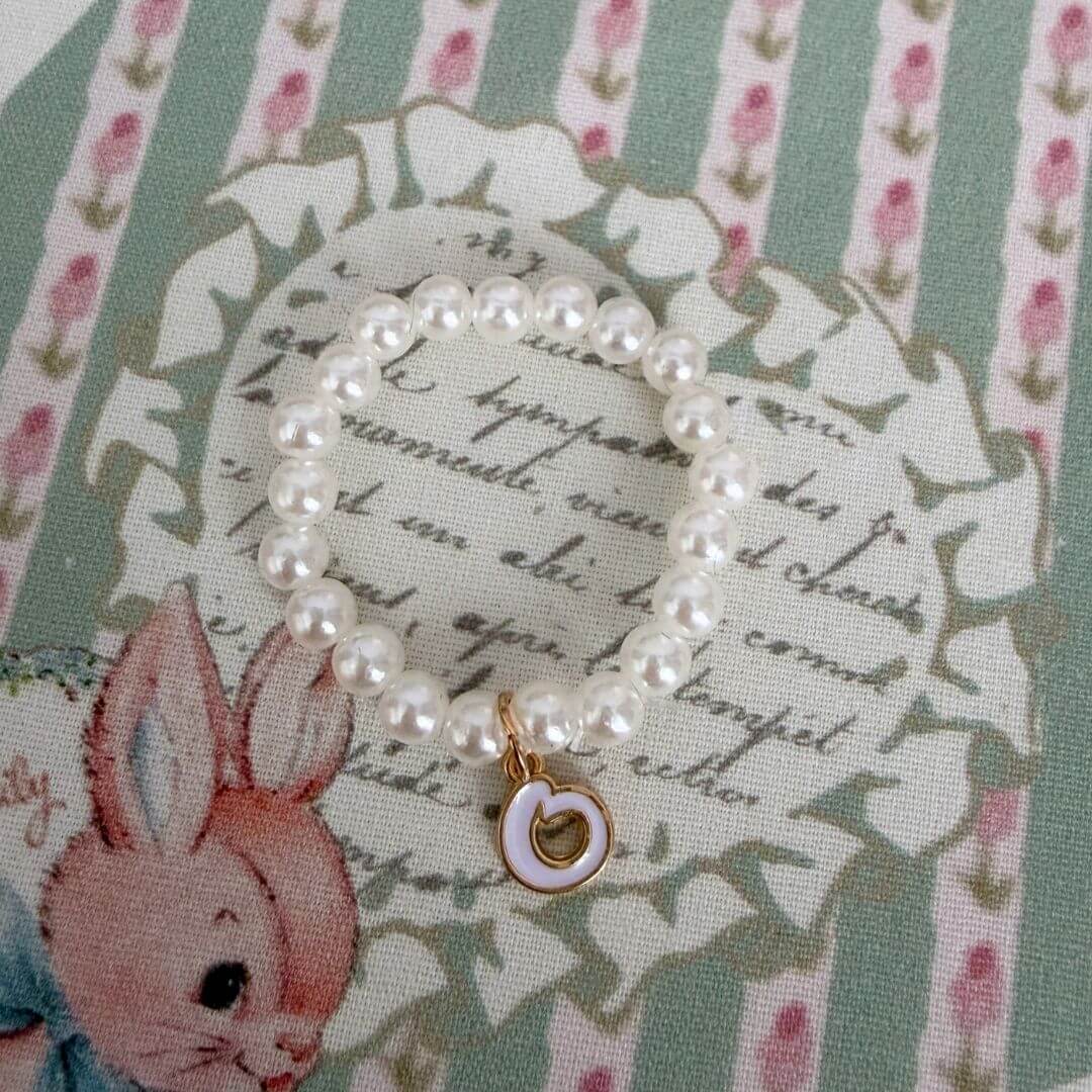 Initial Pearl Necklace featuring faux pearls and a delicate heart charm on a pastel striped background.