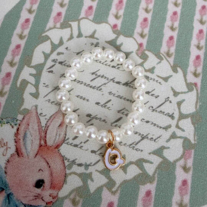 Initial Pearl Necklace with faux pearls and a delicate letter charm, displayed on vintage floral fabric.