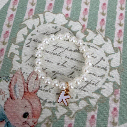 Initial Pearl Necklace featuring faux pearls and a delicate letter 'K' charm on a vintage floral background.