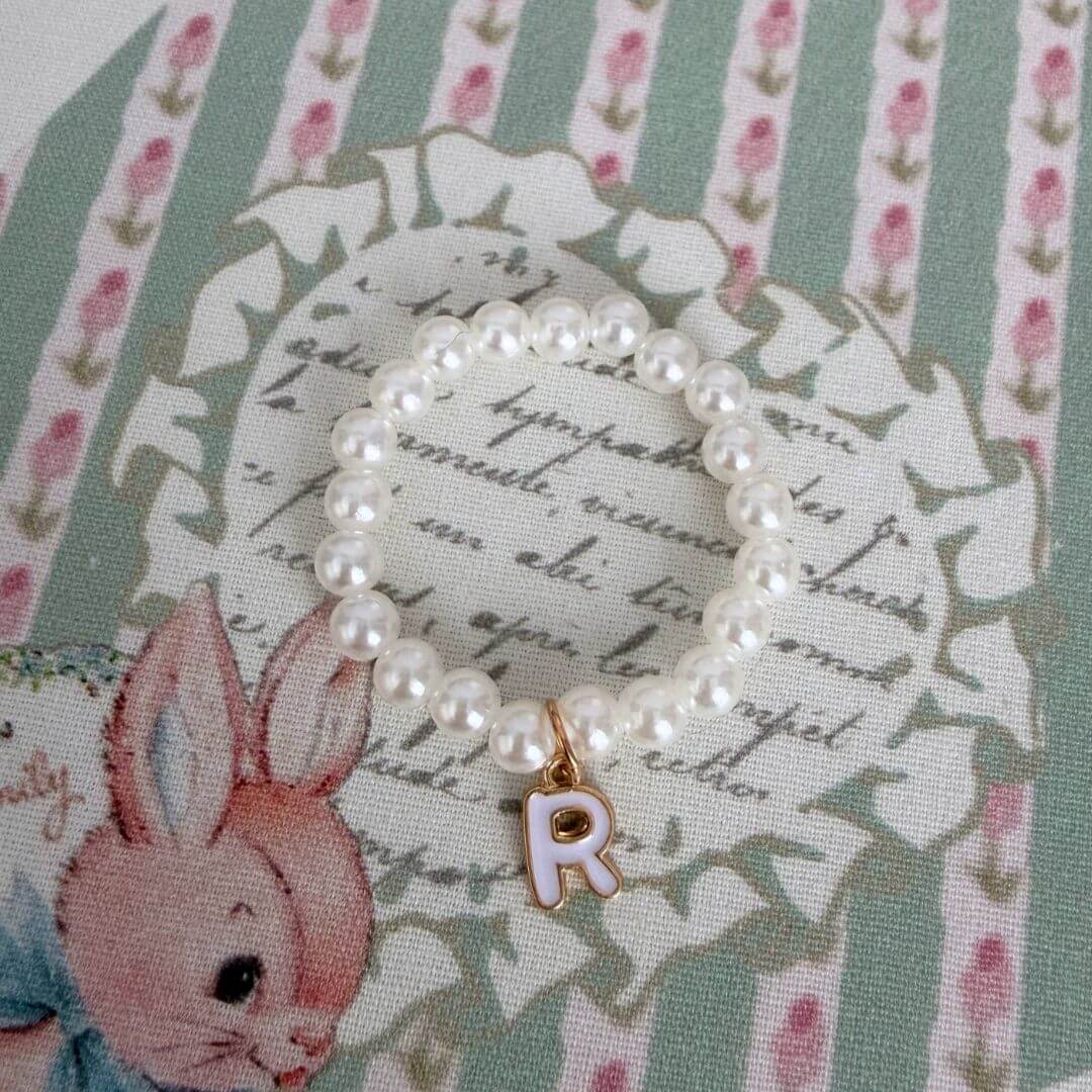 Initial Pearl Necklace with faux pearls and gold letter charm on pastel floral fabric, perfect for a personal touch.