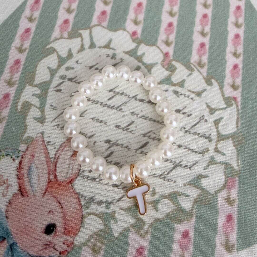 Initial Pearl Necklace featuring delicate faux pearls and a letter 'T' charm, set against a vintage floral background.