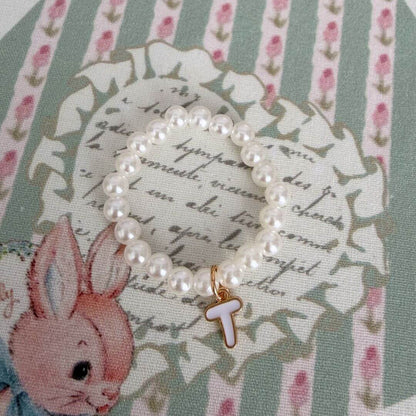 Initial Pearl Necklace featuring delicate faux pearls and a letter 'T' charm, set against a vintage floral background.
